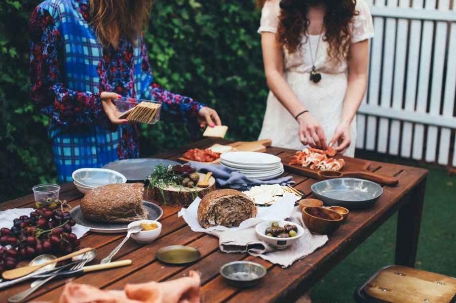 unrecognizable women serving table with assorted appetizers in garden